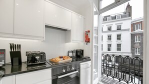 A modern kitchen with white cabinets, a black countertop, and a view of the city through a window. - 10 Curzon Street Apartments by Mansley (London)