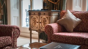 A room with a patterned sofa, a small table with a cup and a book, and a decorative cabinet. - 10 Curzon Street Apartments by Mansley (London)