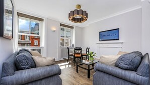 A modern living room with two grey sofas, a coffee table, and a chandelier. - 10 Curzon Street Apartments by Mansley (London)