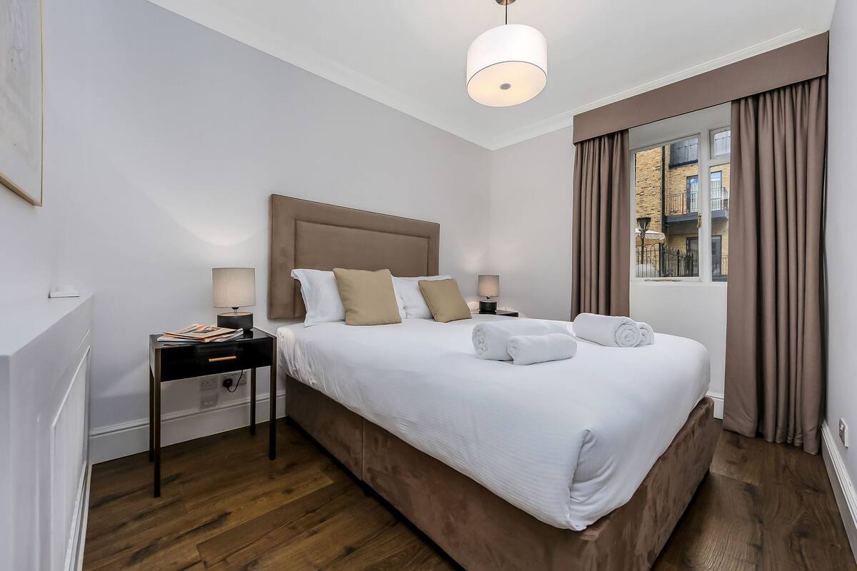 A hotel room with a large bed, two bedside tables, a window with curtains, and a hanging light fixture.