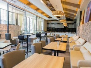 Ein modernes Restaurant mit hohen Decken, Pendelleuchten und einer Mischung aus Sitzgelegenheiten, darunter Tische und gepolsterte Stühle.
