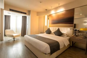 Ein modernes Hotelzimmer mit einem großen Bett, einem Nachttisch, einem Sessel, einem Schreibtisch und einem großen Spiegel.