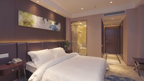 A hotel room with a large bed, a bedside table with a phone, a wall-mounted abstract painting, and a bathroom visible through an open door. - Metropolo Nanjiang Baijia Lake (Nanjing)