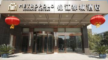The entrance of Jinhua Metropolis Hotel with a modern design, featuring a glass door entrance and red lanterns.