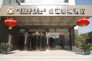 L'entrée de l'hôtel Jinhua Metropolis, avec son design moderne, se distingue par une porte d'entrée en verre et des lanternes rouges.