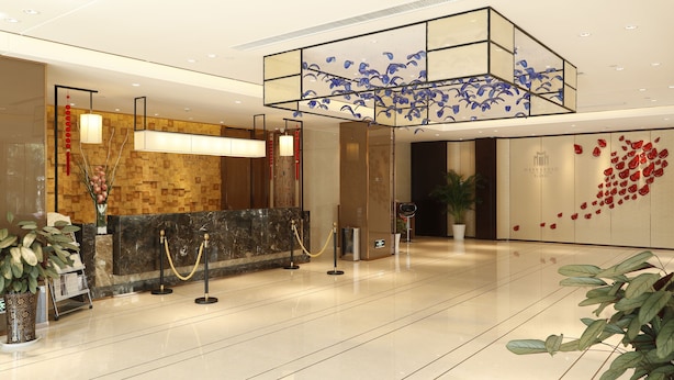 A modern hotel lobby with a reception desk, a decorative ceiling, and a wall with red floral patterns. - Metropolo Nanjiang Baijia Lake (Nanjing)