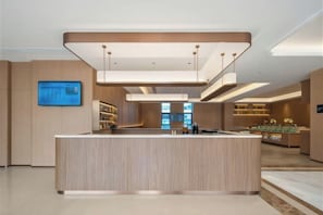 A modern hotel lobby with a central reception desk, a digital display, and a well-lit interior.
