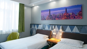 Habitación de hotel con dos camas, una silla verde, un cuadro de un paisaje urbano y una ventana con cortinas.