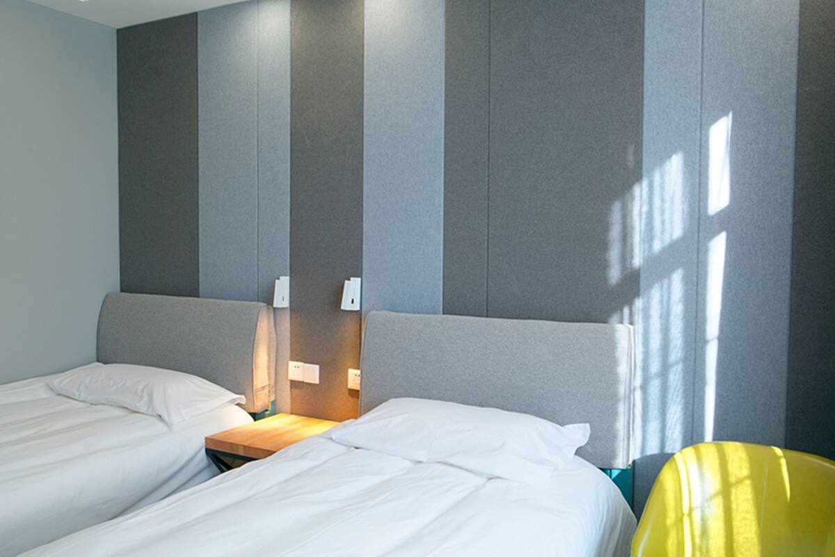 A hotel room with two beds, a wooden nightstand, and a yellow chair.