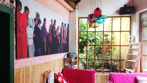 Una habitación con pared de madera, un ventanal con plantas, un sofá rojo, un sofá rosa y una mesa con un jarrón y una lámpara.