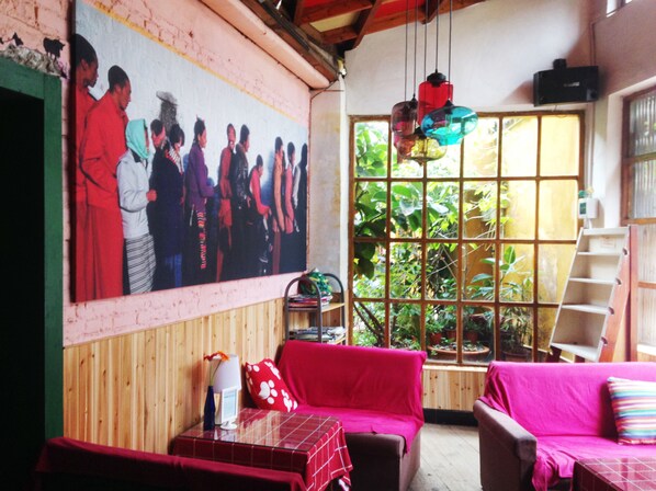 Una habitación con pared de madera, un ventanal con plantas, un sofá rojo, un sofá rosa y una mesa con un jarrón y una lámpara.