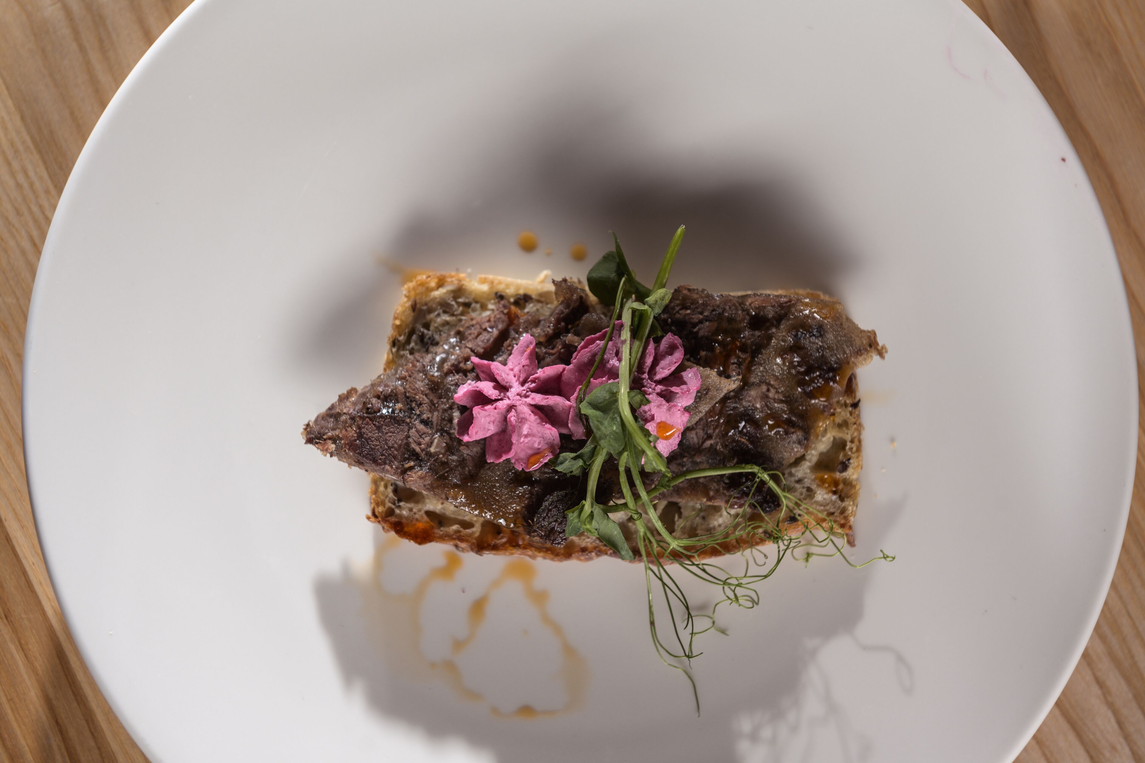 A white plate with a piece of meat and some greens on a wooden table.