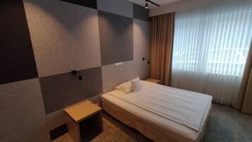 A hotel room with a large bed, a bedside table, a wall-mounted light, and a window with curtains.