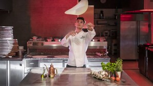 A chef in a white uniform performing a cooking demonstration in a modern kitchen with stainless steel appliances and a red accent wall. - Grape Town Hotel (Zielona Gora)