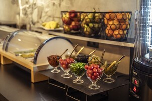 Un bufé con diversos alimentos en recipientes de vidrio, incluyendo frutas y verduras.