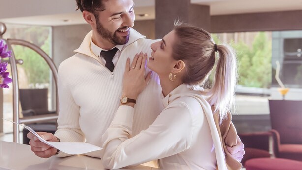 A couple in a modern hotel lobby with a vase of purple flowers on a table. - Grape Town Hotel (Zielona Gora)