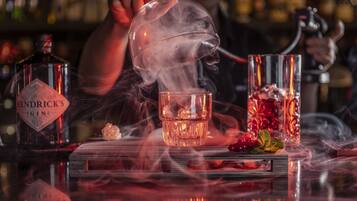 Un bar avec une bouteille étiquetée « Hendrick’s Gin », un verre rempli de glaçons et un récipient décoratif en verre contenant des baies rouges et des feuilles de menthe.