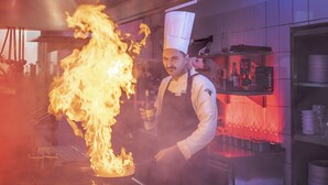 A chef performing a flambé with a bottle of liquor in a kitchen setting. - Grape Town Hotel (Zielona Gora)