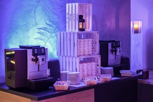 Una estación de café con varias máquinas de espresso, pilas de platos y cestas de pastelería.