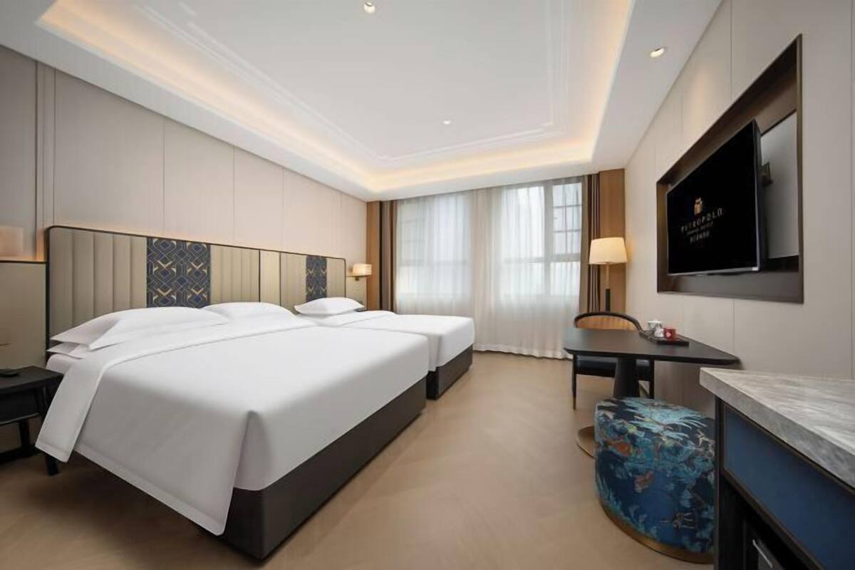 A hotel room with a large bed, a desk, a chair, a TV, and a window with curtains.