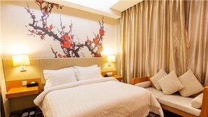 Une chambre d’hôtel avec un grand lit, un canapé, deux tables de chevet et un mur orné d’un tableau représentant des motifs floraux.