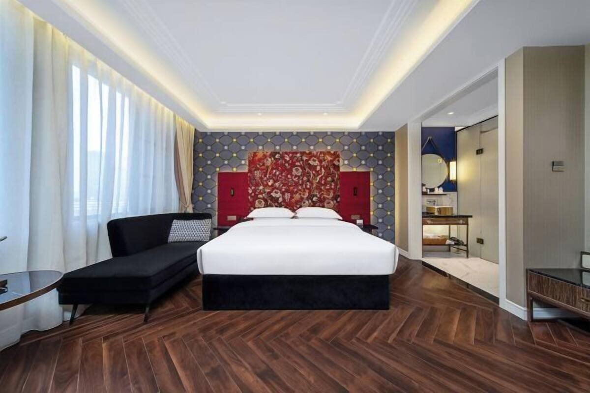A modern hotel room with a large bed, a sofa, a desk, and a bathroom visible through an open door.