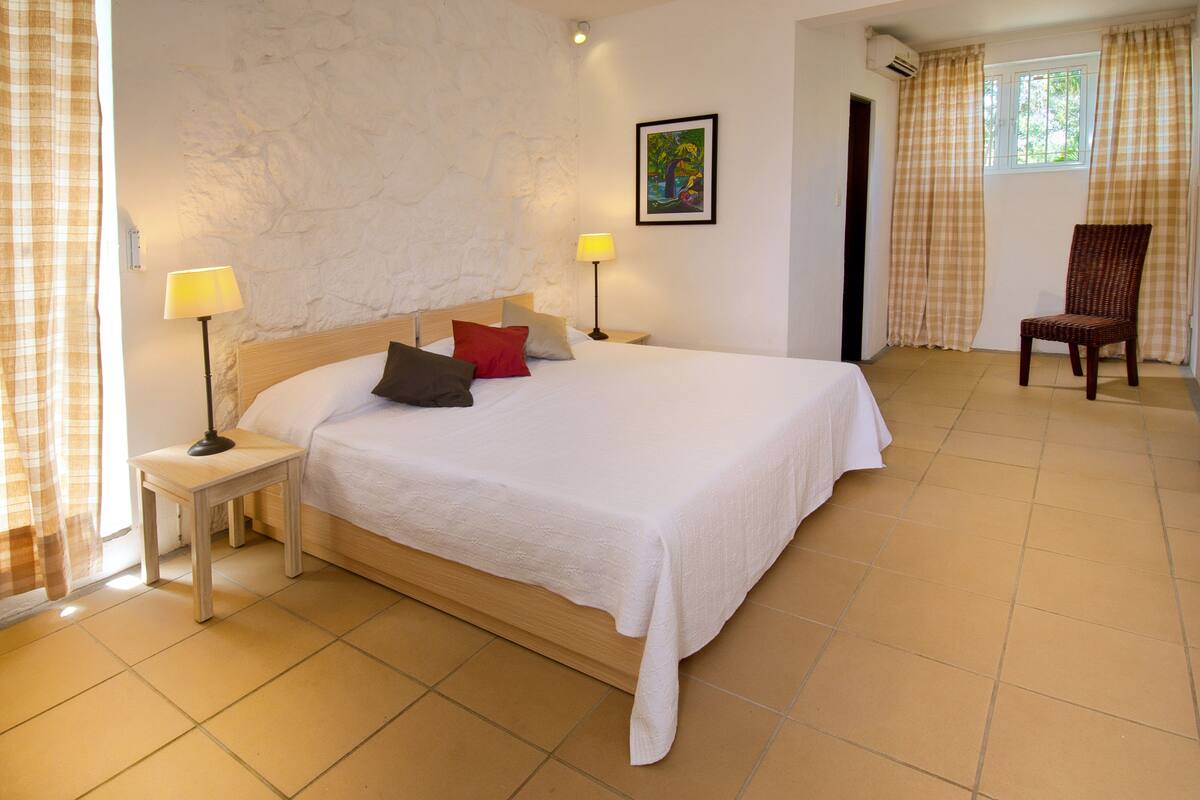 A bedroom with a large bed, two bedside lamps, a chair, a painting on the wall, and a window with curtains.