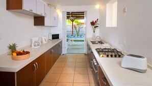 Una cocina moderna con estufa a gas, tostadora y cafetera. Hay una cesta de fruta en la encimera y un florero con flores en la pared.
