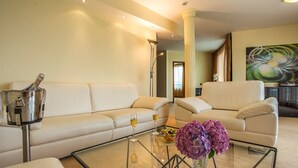 Een moderne woonkamer met een beige bank, een glazen salontafel en een vaas met paarse bloemen.