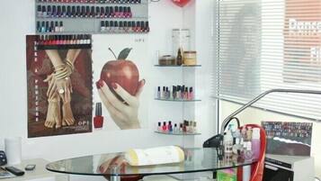 A salon with a red chair, a TV mounted on the wall, nail polish, and a poster of hands holding an apple.