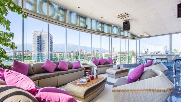 Een moderne lounge met een groot raam en uitzicht over de stad, comfortabele zitplaatsen en een bar.