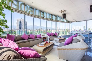 Een moderne lounge met een groot raam en uitzicht over de stad, comfortabele zitplaatsen en een bar.