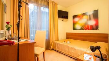 Una habitació d'hotel amb un llit, una taula de treball amb un telèfon, una cadira, una làmpada de taula, un televisor i un quadre a la paret.