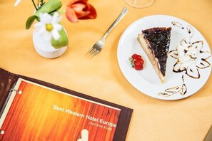 A dessert plate with a slice of pie, a strawberry, and chocolate drizzle on a table with a menu titled "Best Western Hotel Europe". - Europe Hotel Sofia (Sofia)