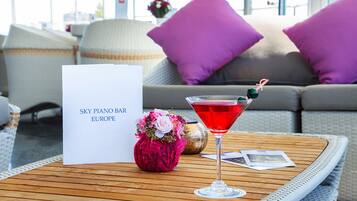 Un cóctel sobre una mesa con una tarjeta que dice "SKY PIANO BAR EUROPE" y un florero decorativo.