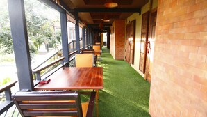 A corridor with wooden tables and chairs, a brick wall, and a green artificial turf path. - Rommai At Home (Prachin Buri)