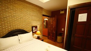 A hotel room with a brick wall, a bed with white linens, a nightstand with a lamp, a wooden wardrobe, and a mirror.