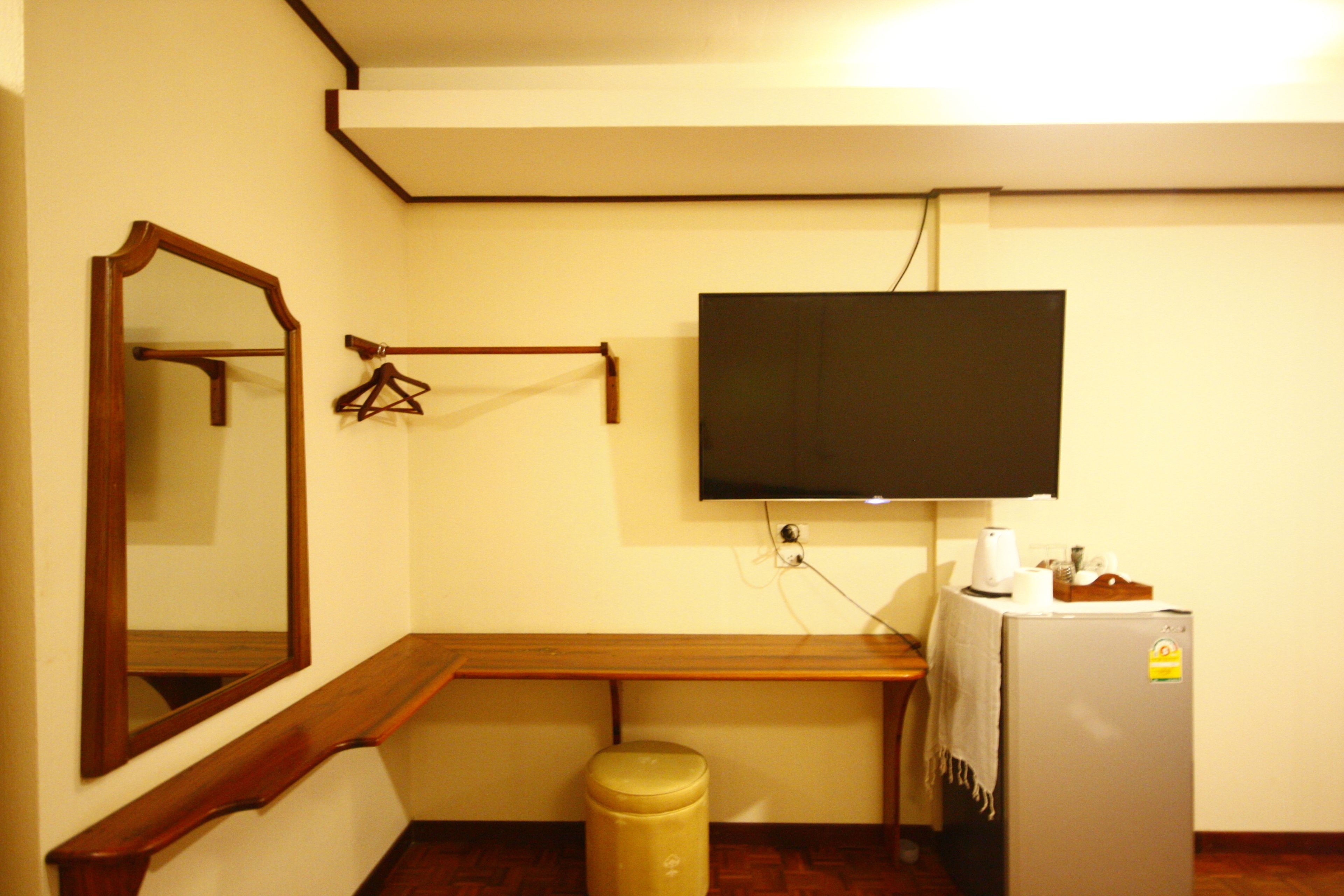 A small room with a wooden bench, a mirror, a television mounted on the wall, and a refrigerator.