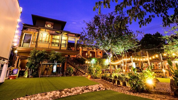 A two-story building with a balcony, a staircase, and a well-lit garden area. - Rommai At Home (Prachin Buri)