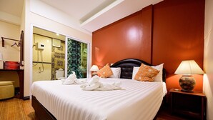 A hotel room with a large bed, a nightstand with a lamp, a bathroom with a shower and toilet, and a view of the outside. - Rommai At Home (Prachin Buri)