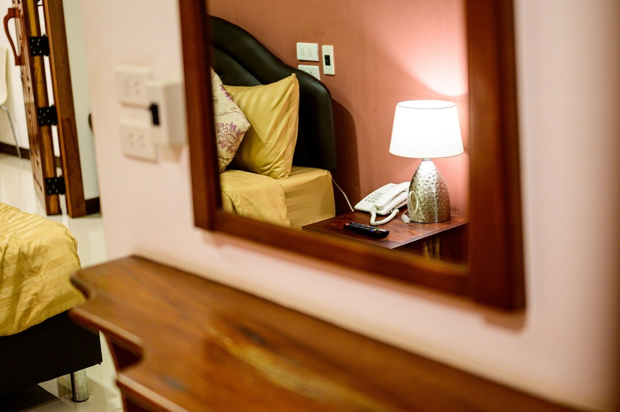Habitación de hotel con cama, mesita de noche, lámpara y un espejo que refleja la cama y la lámpara.