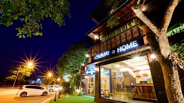 A well-lit hotel entrance with a sign reading "ROMMAI HOME" and a visible reception area.