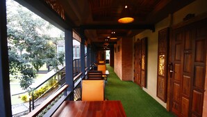 A corridor with wooden benches, a green artificial turf path, and traditional wooden doors. - Rommai At Home (Prachin Buri)