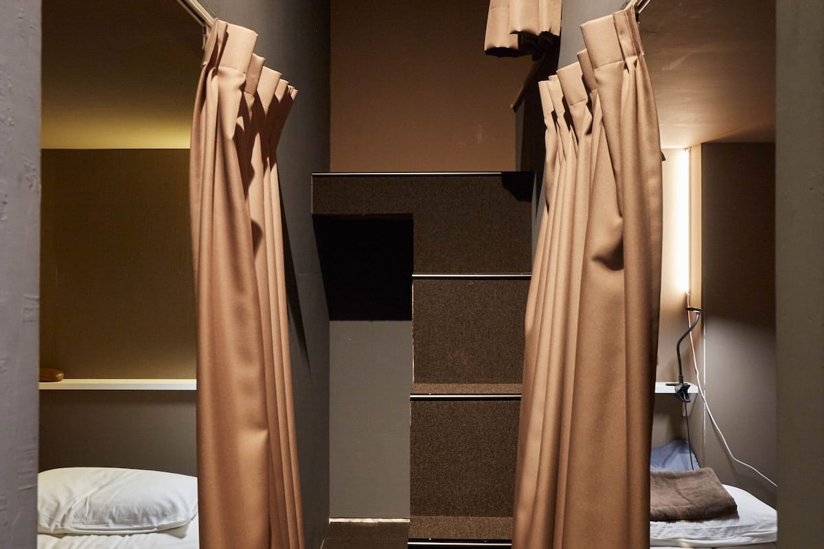 A narrow, dimly lit hallway with two beds on either side, a staircase in the center, and curtains hanging from the ceiling.