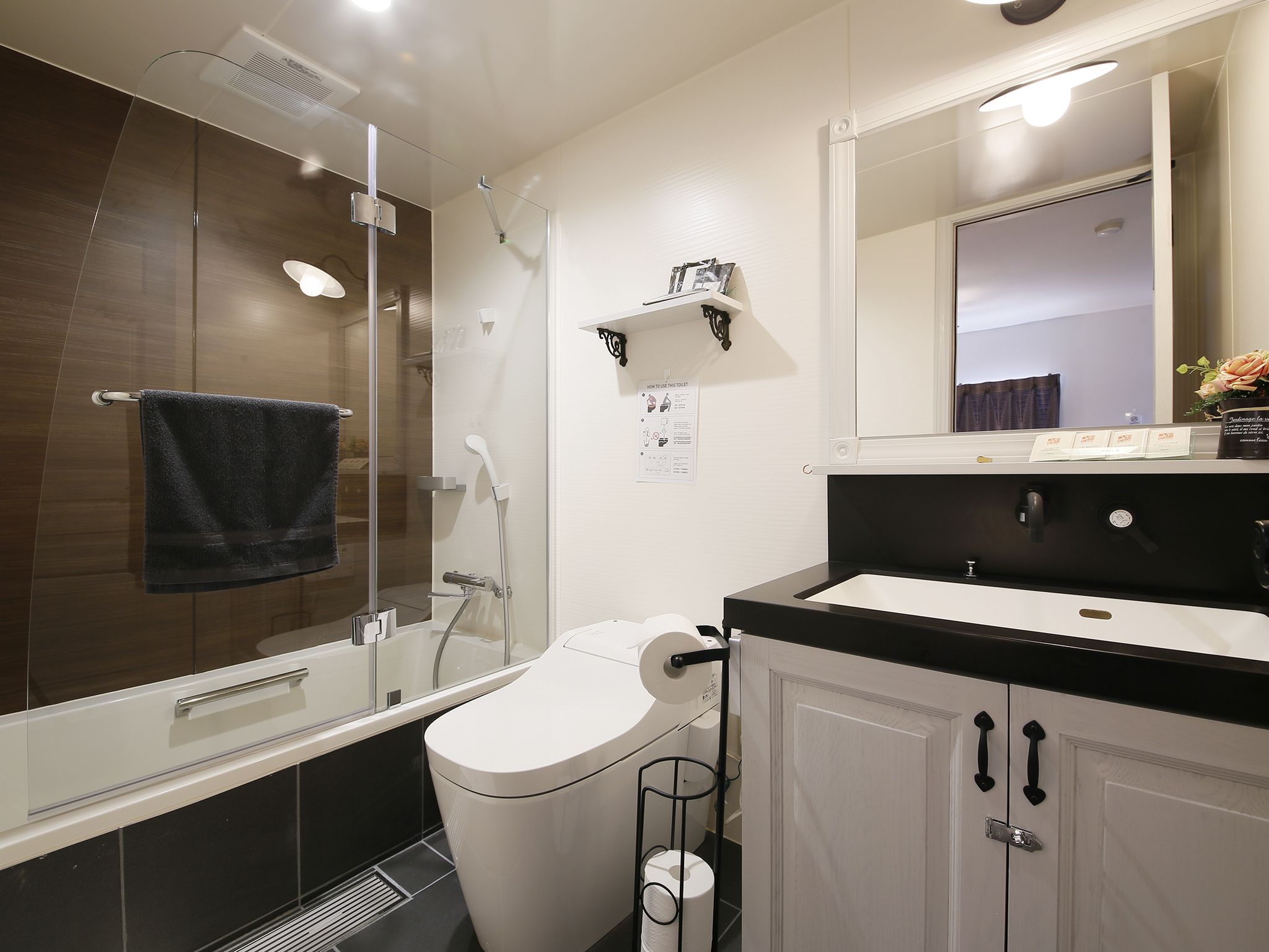 A modern bathroom with a glass shower enclosure, a toilet, a sink with a black countertop, and a mirror above the sink.