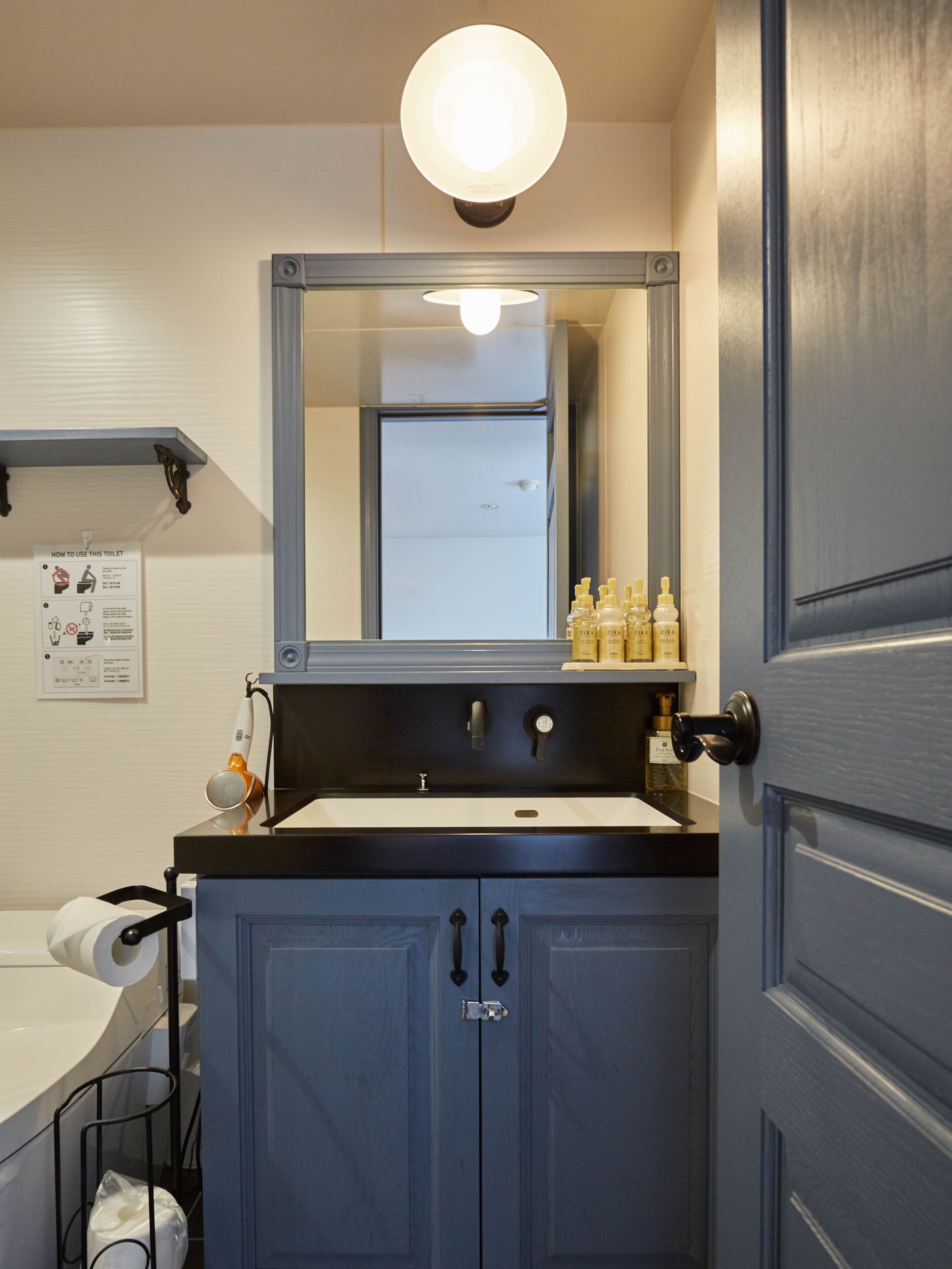 A bathroom with a sink, mirror, and cabinet. There is a sign on the wall and toiletries on the counter.