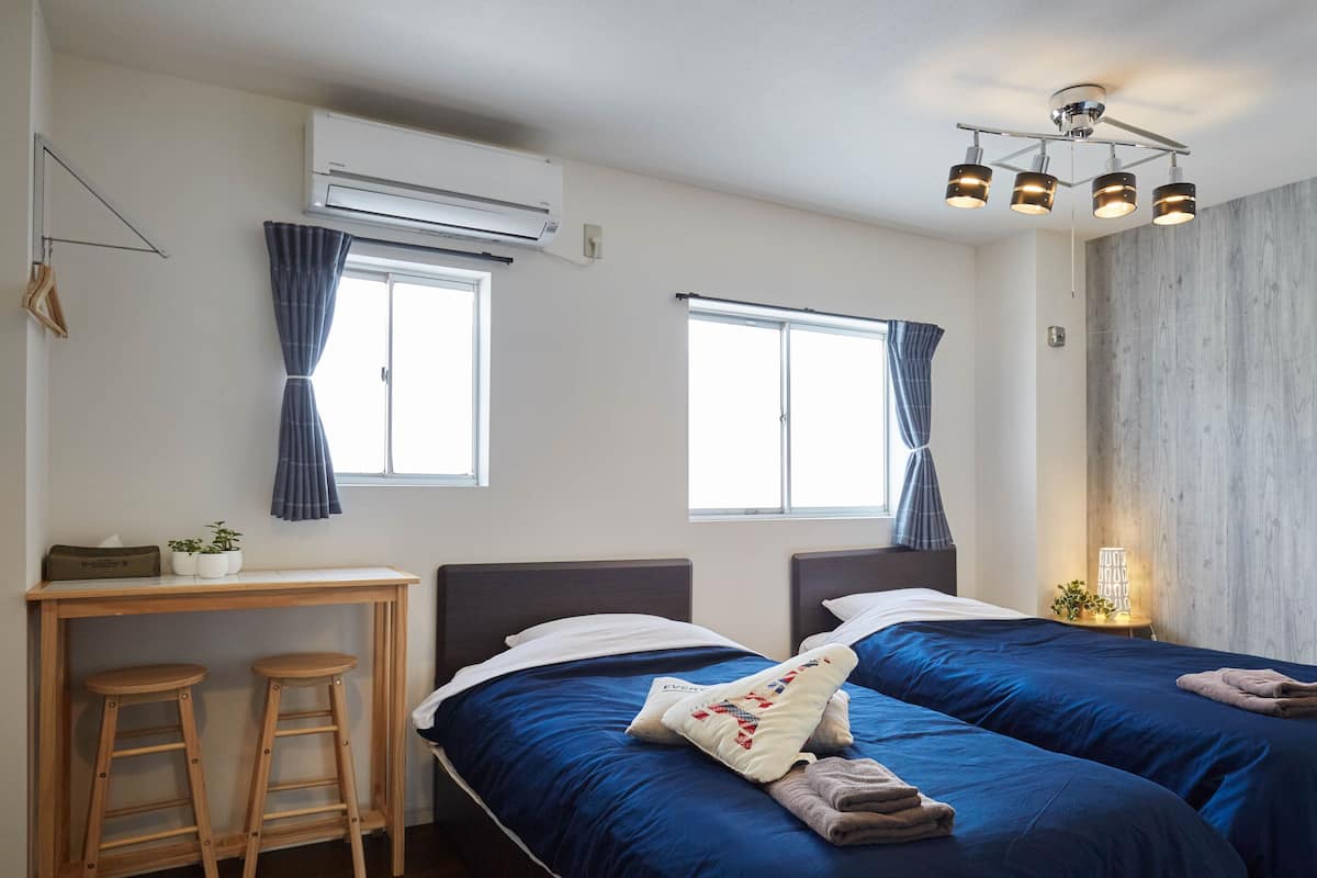 A room with two beds, a desk, and a chair. There is an air conditioner and a ceiling light fixture.