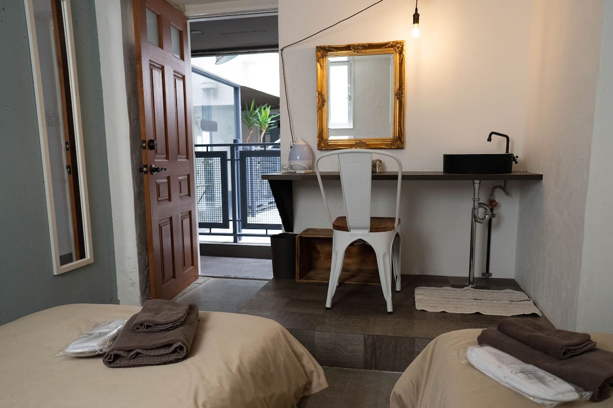 A hotel room with two beds, a desk with a chair, a sink, and a mirror.