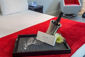 Ein Tablett mit einer Champagnerflasche, Gläsern, einer Karte und einer Blume auf einem roten Teppich in einem modernen Hotelzimmer.