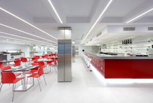 A modern restaurant with red chairs and a stainless steel refrigerator.